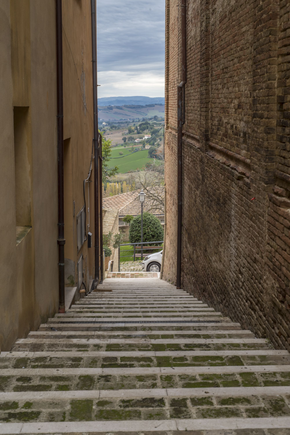 Narrow stairway going down between buildings with a view out to the Italian countryside, Assisi