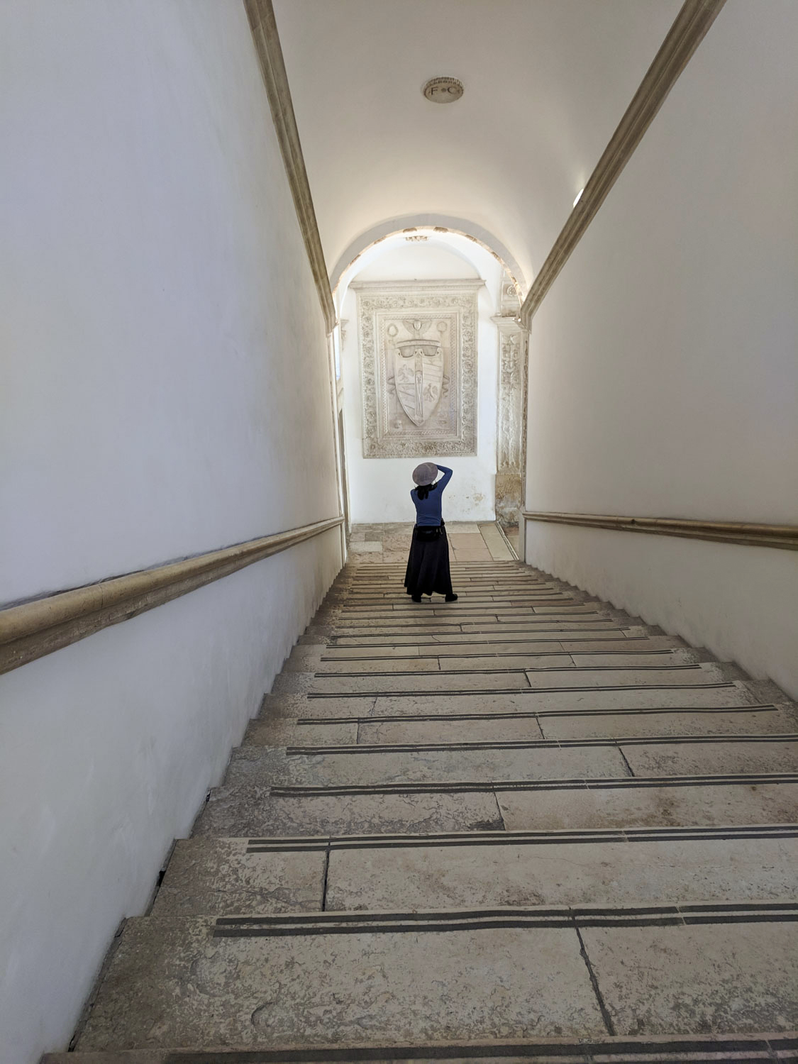 A woman standing with her back to us in a wide stairwell with white walls