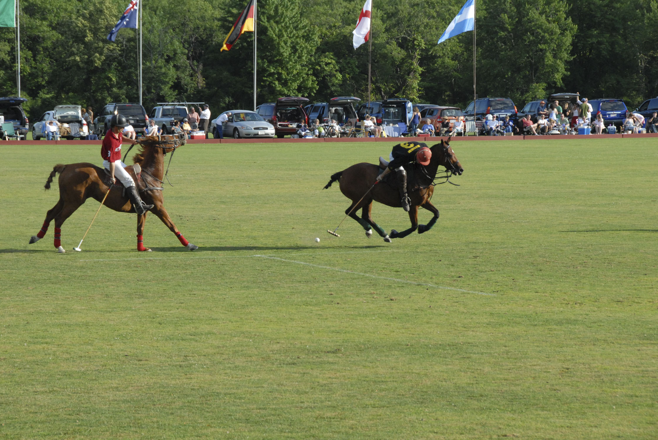 a polo field with two players from opposing teams riding on horseback, one having just struck the ball