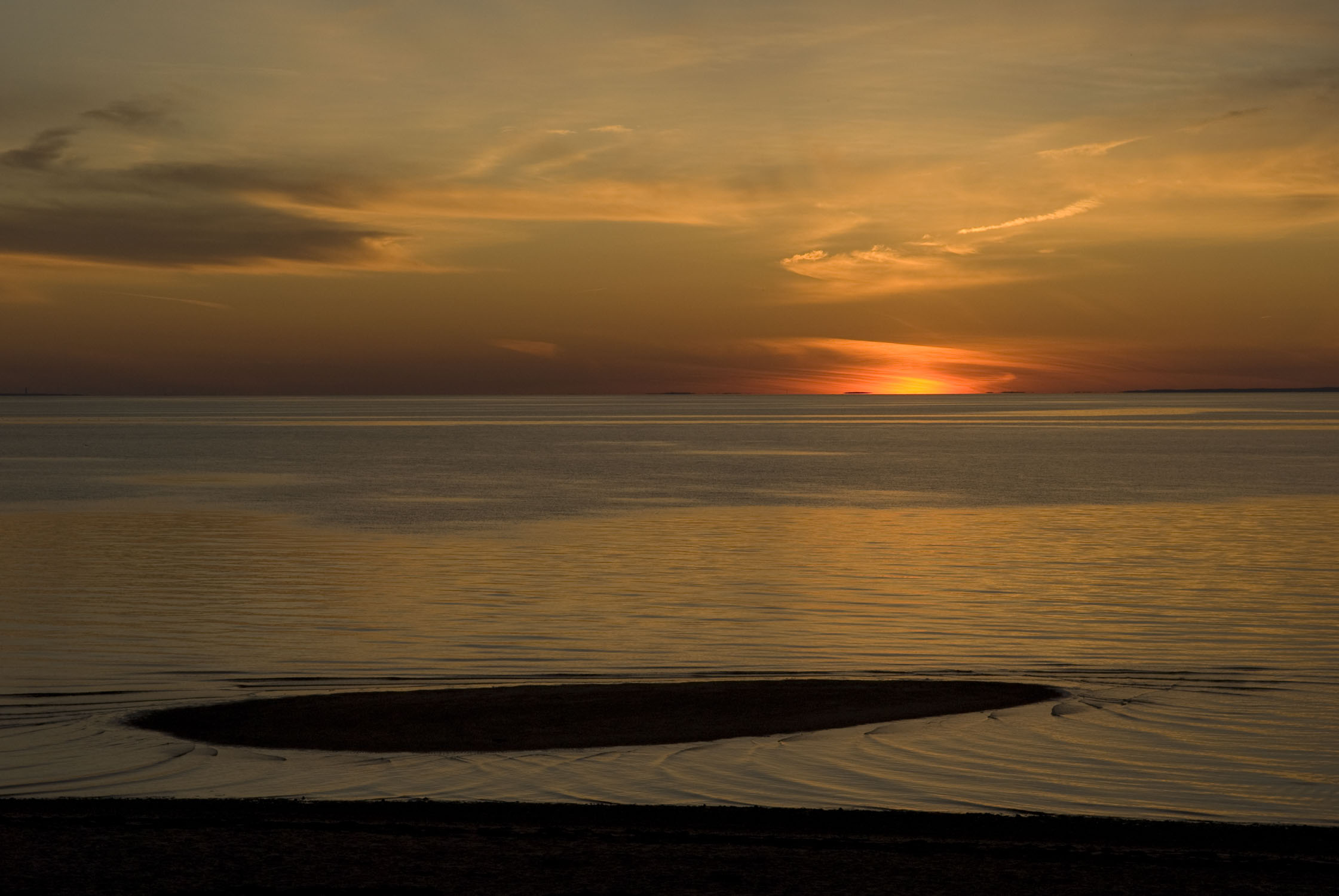 A yellow sky with water that is gently swirling around some sand.