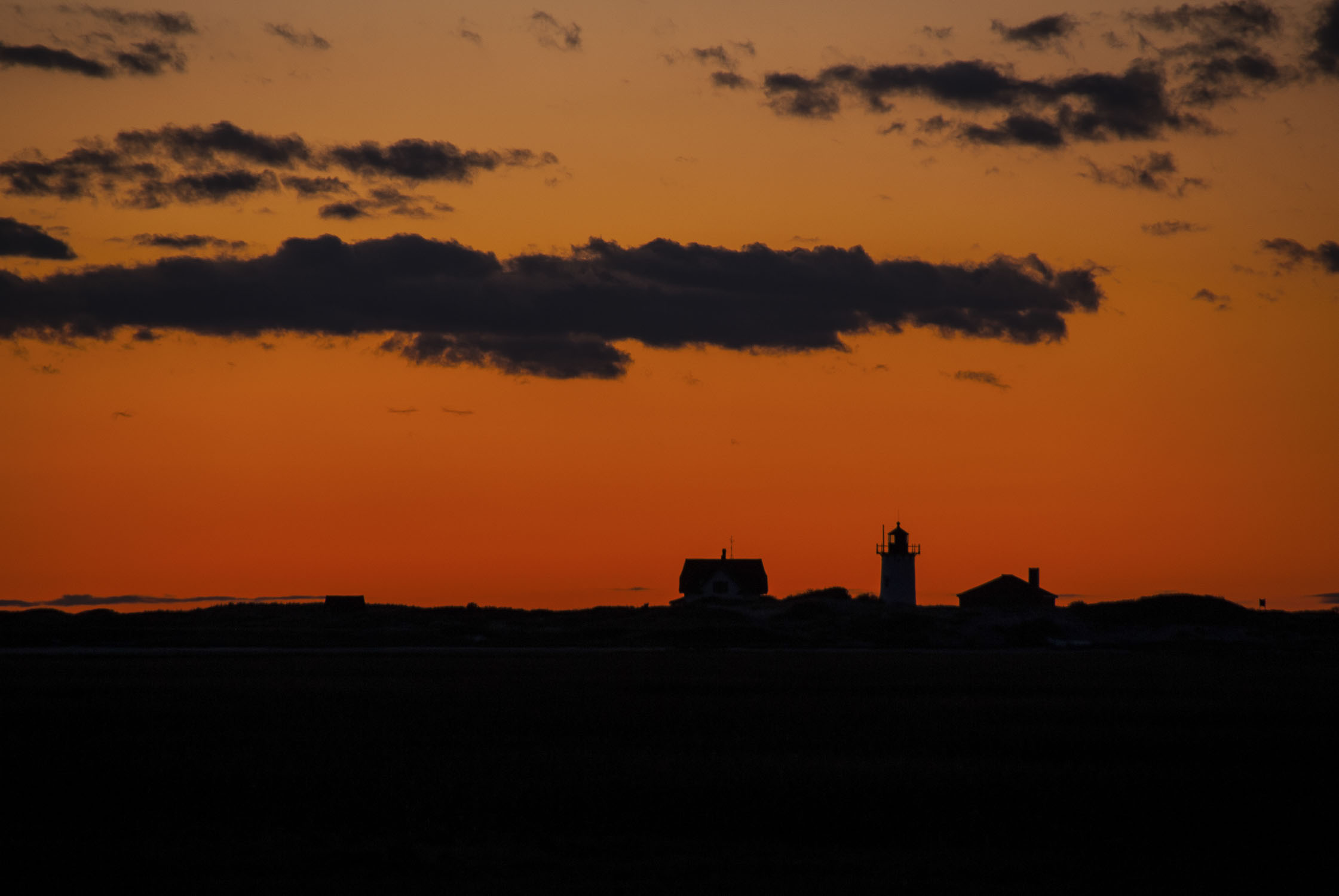 An orange-red sky with the silouhettes of a lighthouse and buildings