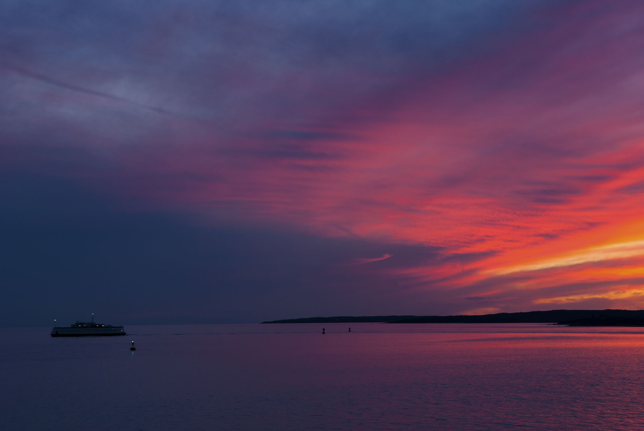 A brilliant pink sky on the right faces to blue on the left, with a ferry in the water.