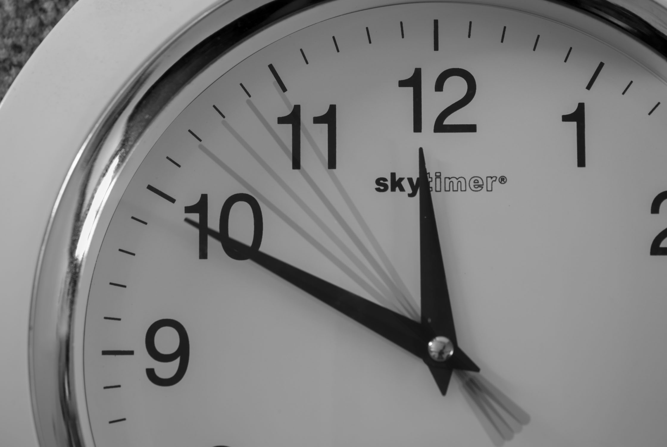 A clock with a silver rimt and bold letters, at 10 of 12, with the second hand moving.