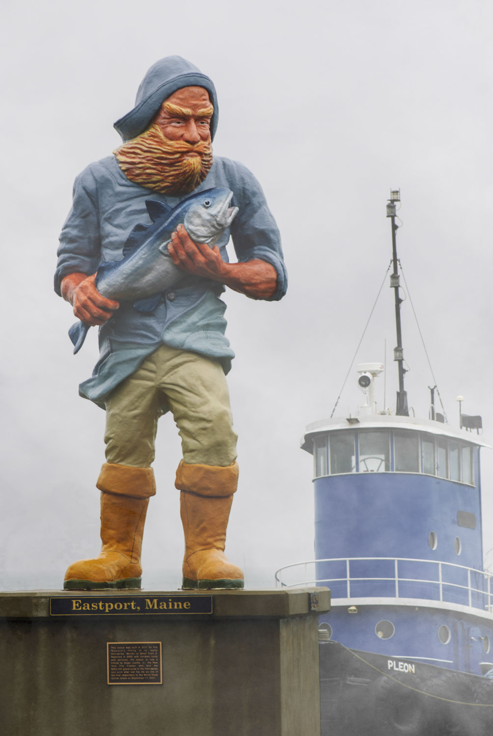 The Eastport fisherman statue with a tugboat behind it