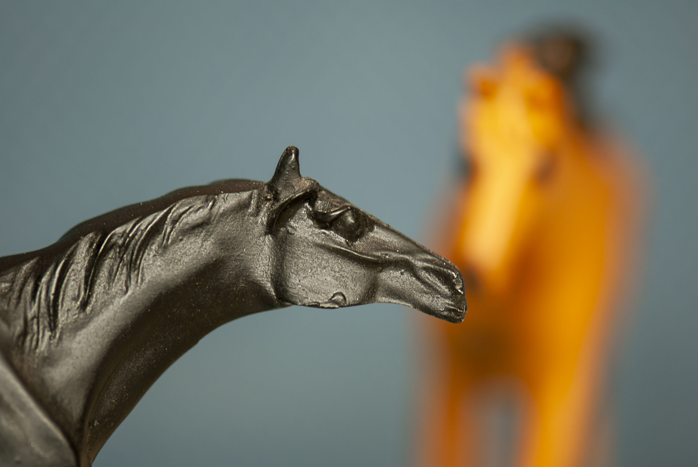 A sculpture of a black horse with a golden brown one out of focus in the background
