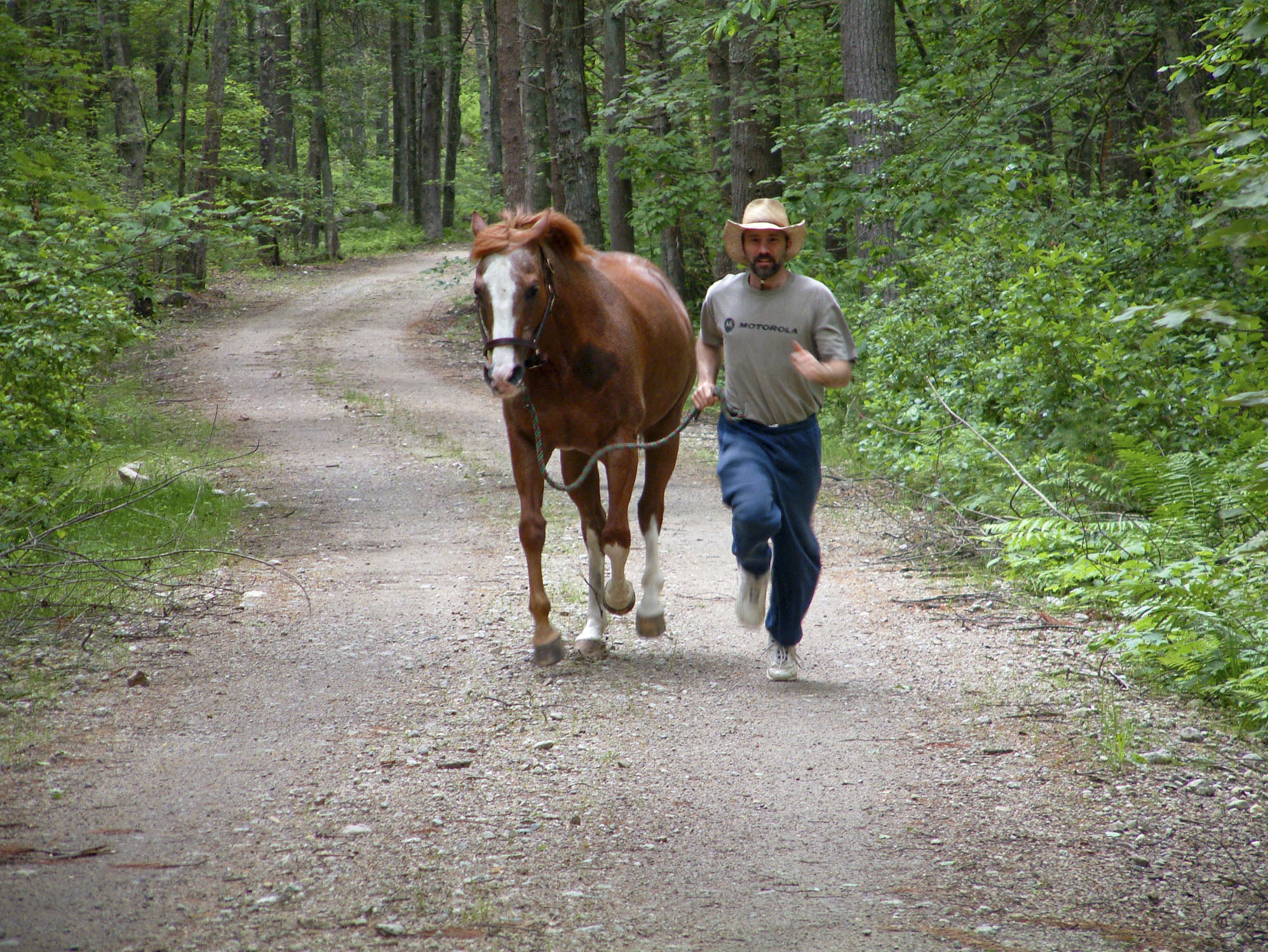 A horse and a man running along side eachother on a dirt road