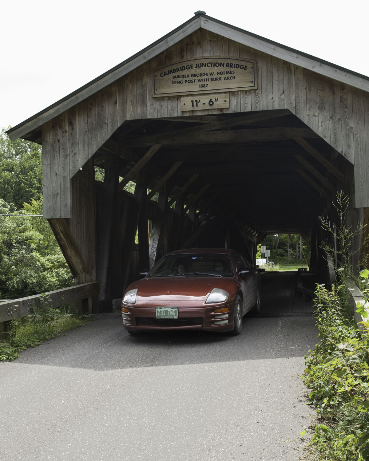 A car is driving out from under a covered bridge.