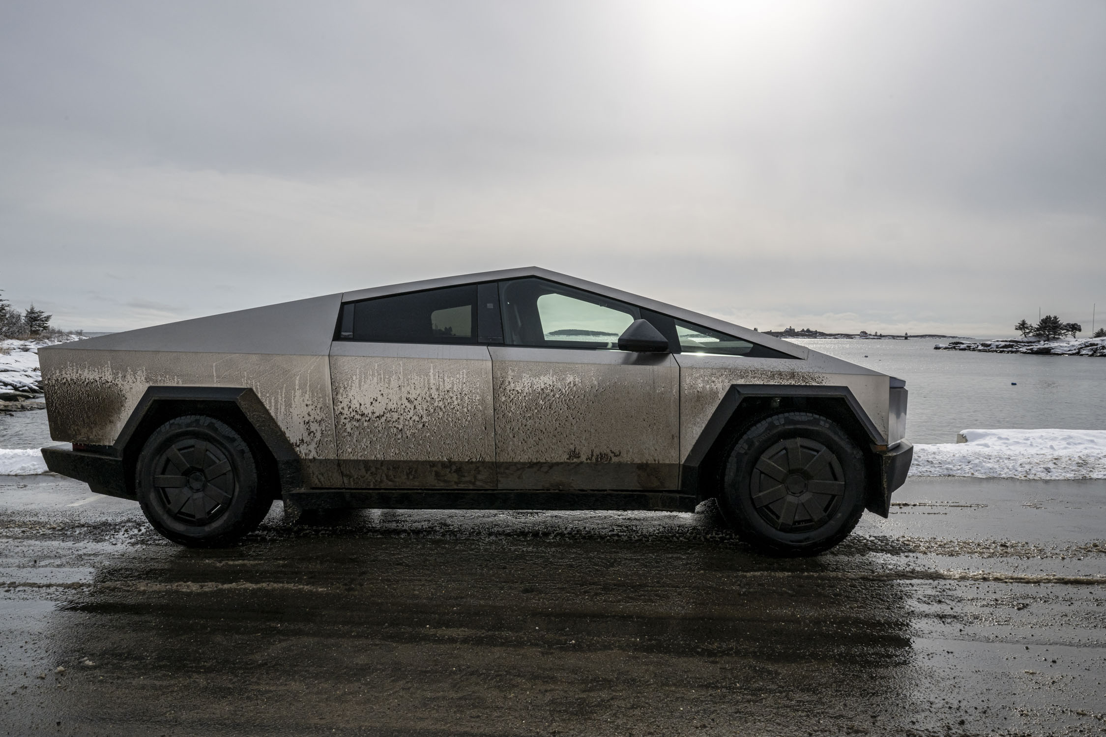 A gray and dirty Cybertruck in front of water