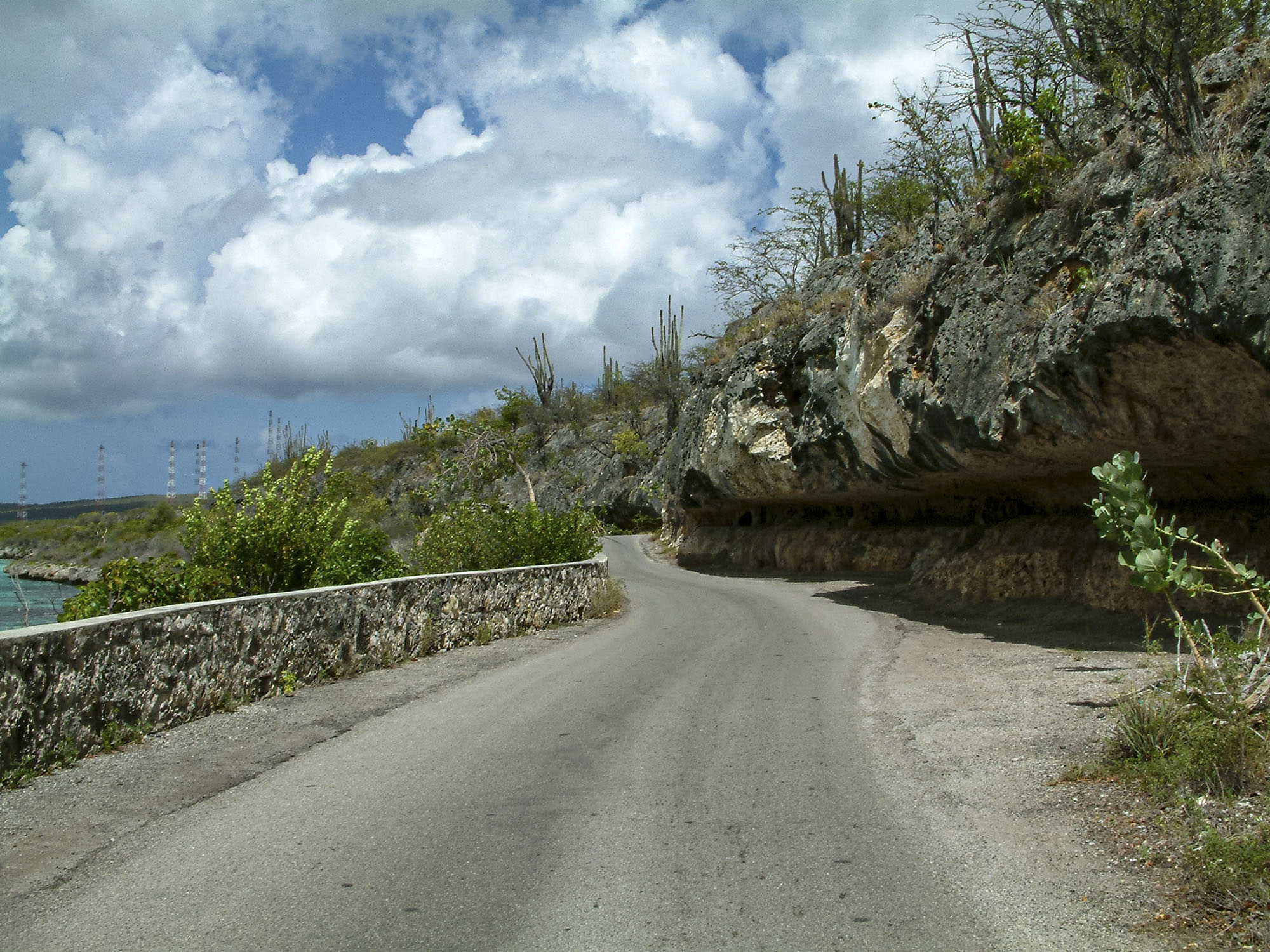 A road along the ocean with rocks overhanging part of the road