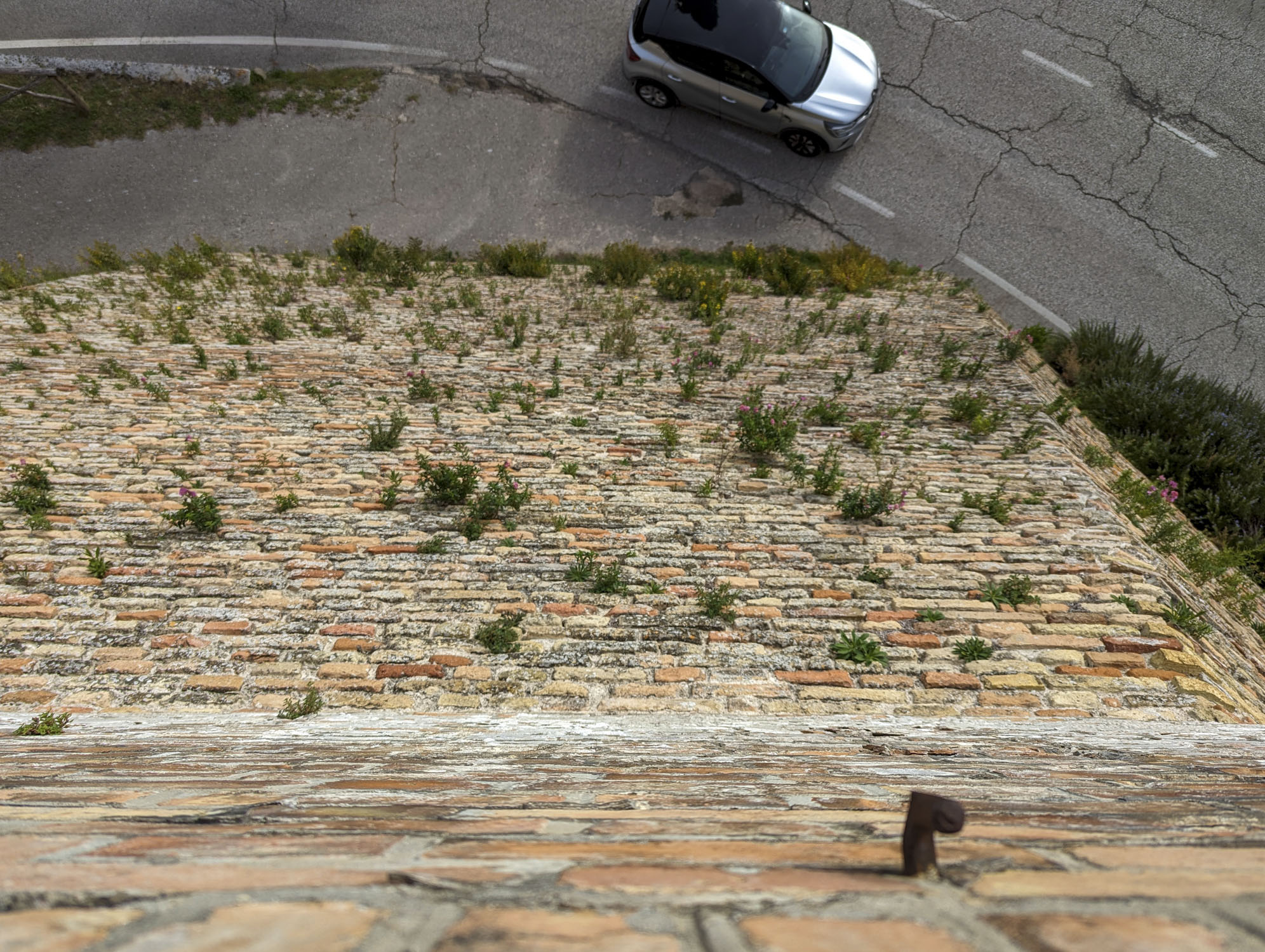 Looking down a very tall stone wall at a car driving on a road.
